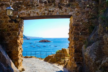 Tossa de Mar 'daki antik kale kapısı, Katalonya, İspanya, Avrupa. Yol, kaya kapısı ve arka planda Akdeniz ve botlar.