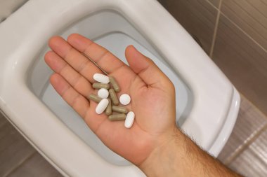 Tuvaletin üzerinde tıbbi tabletleri olan bir erkek. Karın ağrısı, kabızlık, ishal veya gıda zehirlenmesi konsepti..
