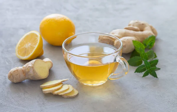 Transparent cup of healthy hot ginger tea with mint and lemon on stone table