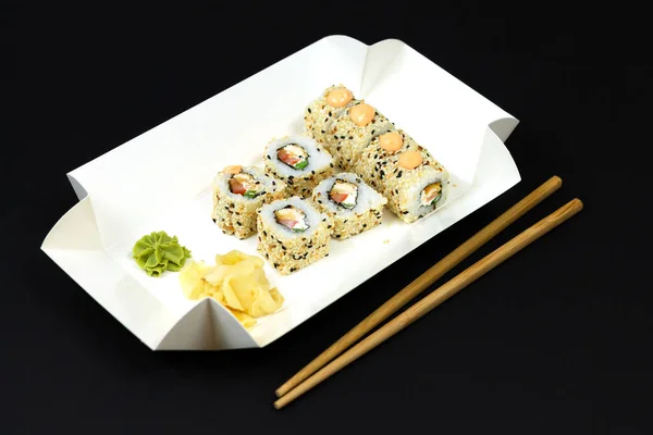 Japanese sushi rolls in white eco paper disposable box on dark background close-up