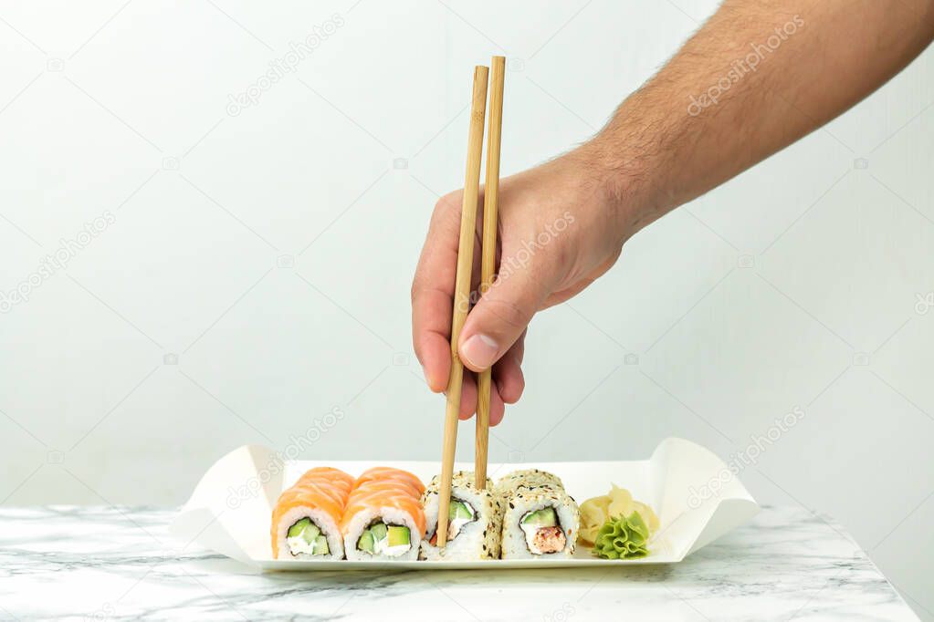 Man holding chopsticks and eating Japanese sushi set at home. Take away delivery service concept