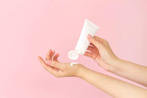 Kadın elleri pembe arka plana kozmetik cilt bakım nemlendirici kremi sürerler.