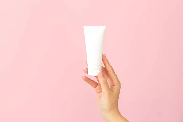 Kadın elinde krem tüpü tutuyor ve güzel ellerine nemlendirici sürüyor. Pembe arka planda yumuşak ve sağlıklı bir cilt için.