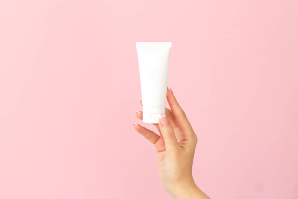 Woman holding cream tube and applying moisturizer lotion on her beautiful hands for soft and healthy skin on pink background