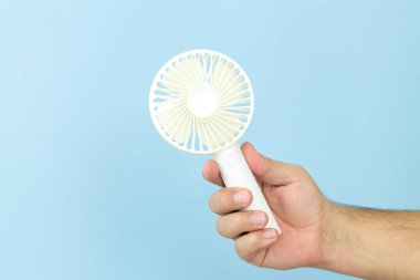 Elinde küçük taşınabilir USB fan tutan adam mavi arka planda izole edilmiş.