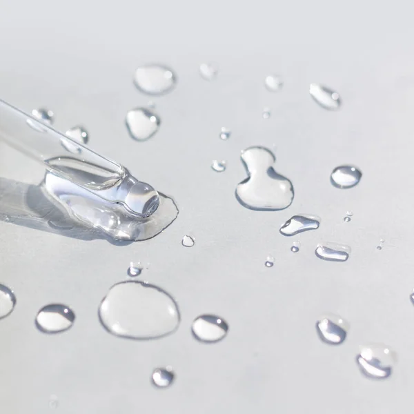 Gri arkaplanda damlaları olan şeffaf jel ya da serum pipeti