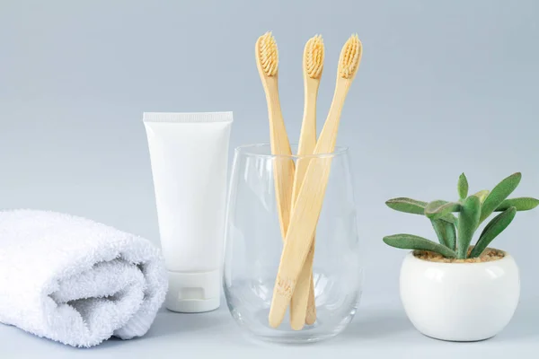 Glass with family set of eco biodegradable bamboo toothbrashes next to toothpaste, towel and green plant