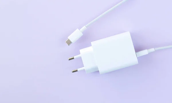 Mobile phone charger for fast charge through USB cable on purple background top view