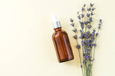 Kurumuş lavanta çiçeklerinin yanına konmuş kahverengi organik lavanta yağı şişesi ya da serum.