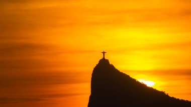 Rio de Janeiro, Brezilya: 2021 - Cristo Redentor 'un (Kurtarıcı İsa) açık turuncu gökyüzü ile günbatımında geniş bir görüntüsü