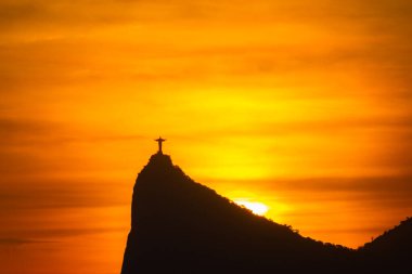 Rio de Janeiro, Brezilya: 2021 - Cristo Redentor 'un (Kurtarıcı İsa) açık turuncu gökyüzü ile günbatımında geniş bir görüntüsü