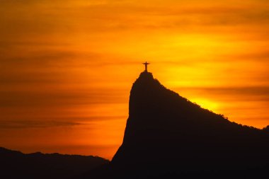 Rio de Janeiro, Brezilya: 2021 - Cristo Redentor 'un (Kurtarıcı İsa) açık turuncu gökyüzü ile günbatımında geniş bir görüntüsü