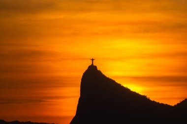 Rio de Janeiro, Brezilya: 2021 - Cristo Redentor 'un (Kurtarıcı İsa) açık turuncu gökyüzü ile günbatımında geniş bir görüntüsü