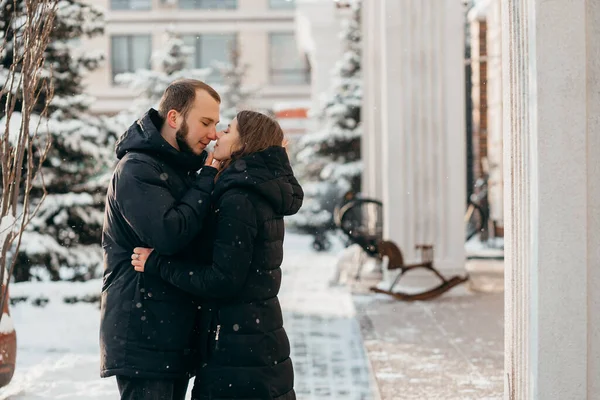 El chico besa suavemente a la chica contra el fondo de la ciudad nevada — Foto de Stock