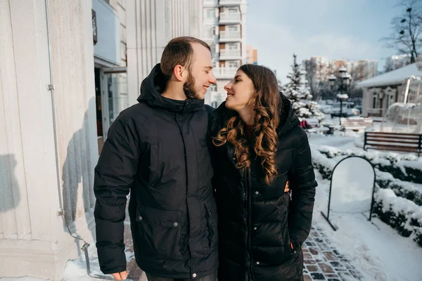 Cara e menina feliz caminham pela cidade coberta de neve e sorriem ternamente um para o outro — Fotografia de Stock