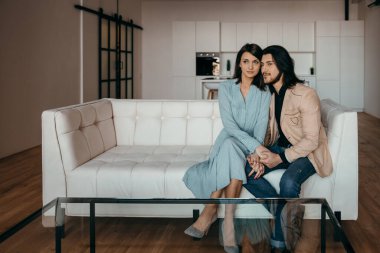 Evli bir çift yeni evlerinde lüks beyaz bir kanepede oturuyor.