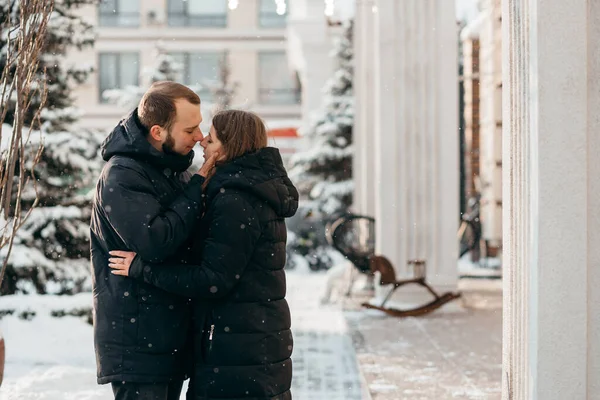 El chico besa suavemente a la chica contra el fondo de la ciudad nevada — Foto de Stock