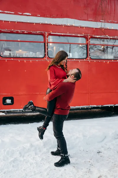 El tipo levantó a la chica en sus brazos y la rodea contra el fondo de un autobús rojo — Foto de Stock