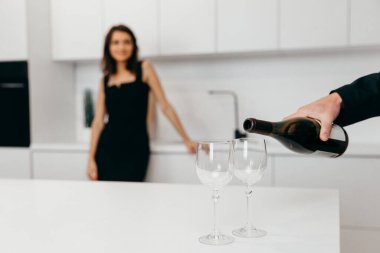 Bir adam kırmızı şarabı bardaklara doldurur. Arkadaki kadın.