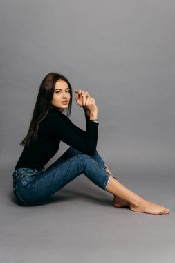 Stüdyoda gri bir zeminde oturan güzel vücutlu harika bir genç kız..