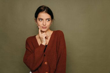 Genç, kısa saçlı esmer kadın. Sol taraftaki fotokopi odasına bakıp eliyle çenesini desteklemeyi düşünüyor..