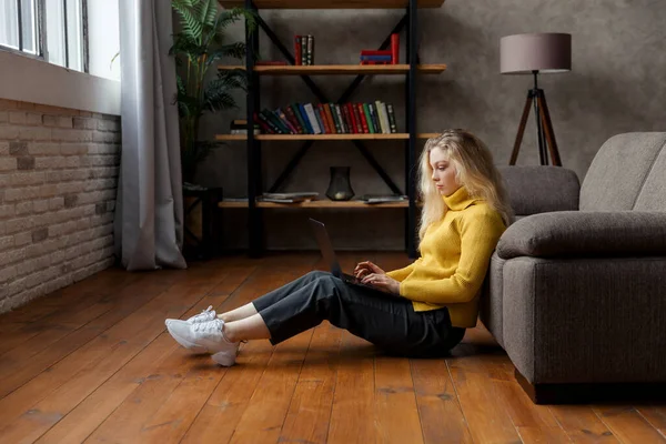 Молода жінка сидить на підлозі вдома і працює з ноутбуком . — стокове фото