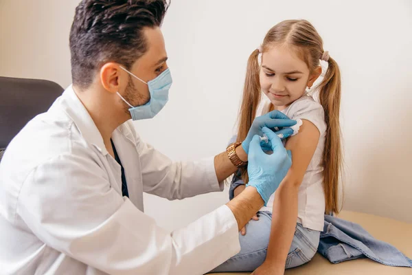 En arabisk eller tyrkisk læge giver en lille pige en coronavirus vaccine. Pige smiler Stock-foto