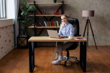 Ofisteki bilgisayarı ve laptopu kullanarak başarılı bir şekilde gülümseyen genç iş kadını..