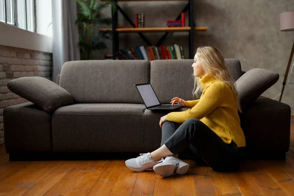 Молода жінка сидить на підлозі вдома і працює з ноутбуком . — стокове фото