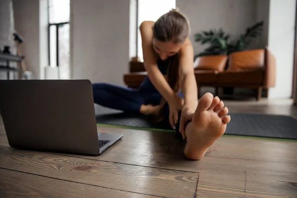 Jovem praticando ioga online, cabeça a joelho asana na sala de estar. Janu Sirsasana posar. Foco no pé. — Fotografia de Stock
