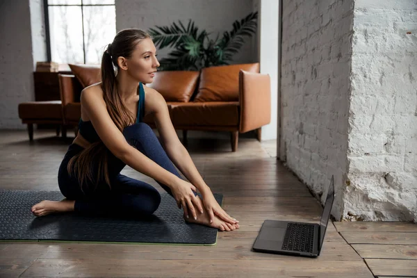 Mulher fazendo exercícios de fitness no tapete oposto laptop em casa. Bem-estar e conceito de estilo de vida saudável. — Fotografia de Stock