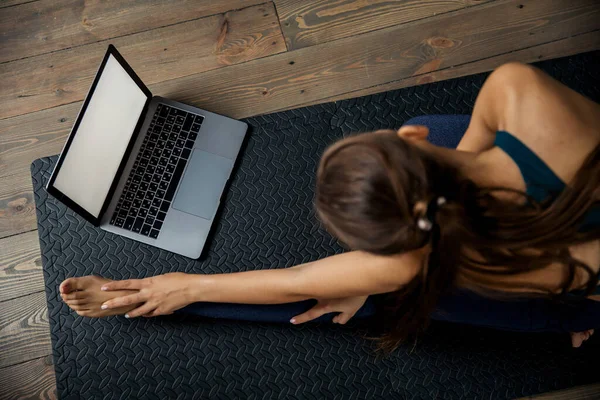 Feminino praticando ioga ou pilates dentro de casa no tapete, fazendo exercícios e alongamento, assistindo vídeo aula on-line. Vista superior — Fotografia de Stock