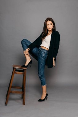 Uzun saçlı, ceketli ve kot pantolonlu esmer kadın ayağını sandalyenin arkasına koydu.