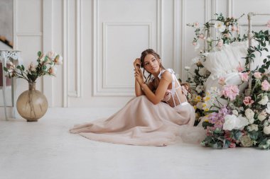 Pembe gelinlikli güzel gelin yatağın yanında çiçeklerle oturuyor.