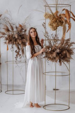 Beyaz boho elbiseli güzel bir kız çiçekliğin yanında duruyor.