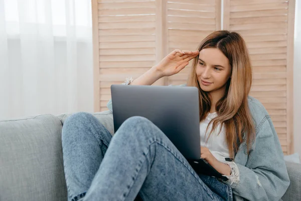 Mujer feliz tumbada en el sofá en casa y mirando a la pantalla de la computadora viendo webinar o haciendo chat de vídeo por webcam. — Foto de Stock
