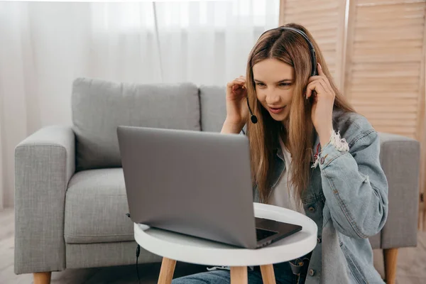 Усміхнена молода дівчина-підліток носить навушники і дивиться на екран комп'ютера, дивлячись вебінар або роблячи відеочат через веб-камеру — стокове фото
