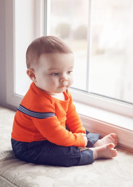 Portrait of cute adorable Caucasian baby boy sitting on windowsi — Stockfoto