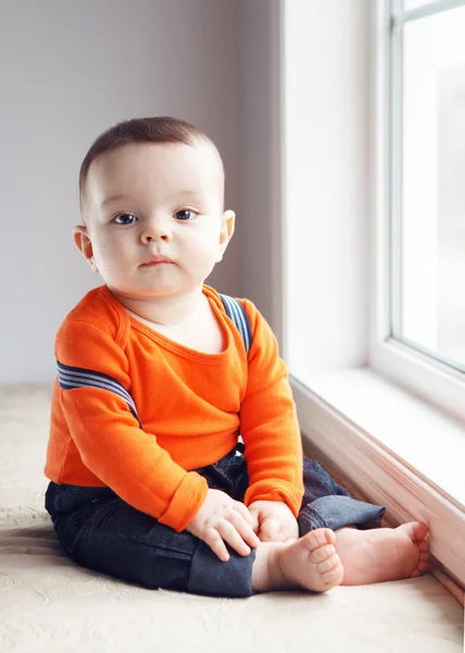 Portrait of cute adorable Caucasian baby boy sitting on windowsi Stockbild