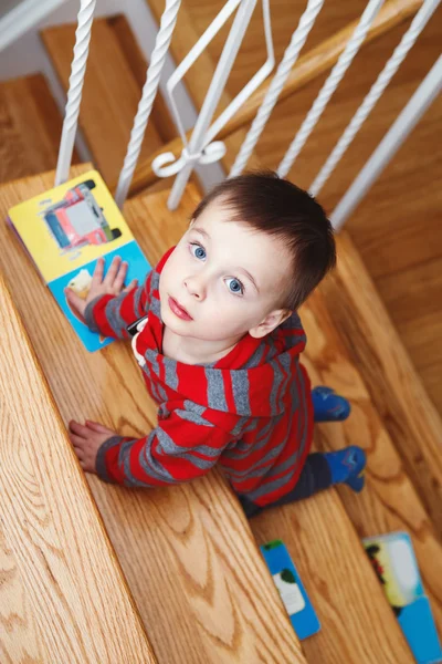 Potret anak laki-laki kecil yang lucu berusia dua tahun dengan buku anak-anak memanjat tangga di dalam rumah melihat ke atas, ditembak di atas kepala di atas — Stok Foto