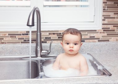 Oturan büyük evye su ve kamera, pencereden bakarak yakınındaki köpük ile yaşam tarzı her gün kavramı koyu siyah gözlü sevimli beyaz komik bebek kız çocuk portresi