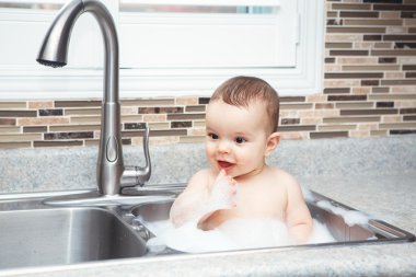Oturan büyük evye su ve köpük, pencereden bakarak yakın yaşam tarzı her gün kavramı koyu siyah gözlü sevimli beyaz komik bebek kız çocuk portresi