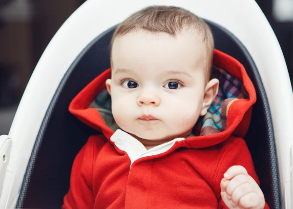 Foto close-up dari cute adorable Caucasian little baby boy dengan mata hitam gelap duduk di kursi tinggi di dalam ruangan melihat ke kamera — Stok Foto