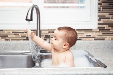 Oturan büyük evye su ve köpük, pencereden bakarak yakın yaşam tarzı her gün kavramı koyu siyah gözlü sevimli beyaz komik bebek kız çocuk portresi