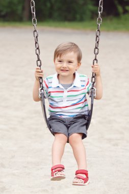 Portrait of happy smiling little boy toddler in tshirt and jeans shorts on swing on backyard playground outside on summer day, happy childhood lifestyle concept