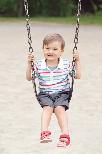 Portrait of happy smiling little boy toddler in tshirt and jeans shorts on swing on backyard playground outside on summer day, happy childhood lifestyle concept — 图库照片