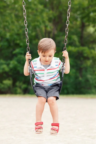 Portret cute little mały chłopiec maluch patrząc od, noszenie tshirt i dżinsy szorty na huśtawce na podwórku plac zabaw na zewnątrz w letni dzień, szczęśliwy styl życia z dzieciństwa — Zdjęcie stockowe