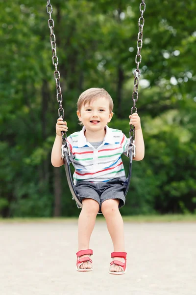 Portrait of happy smiling little boy toddler in tshirt and jeans shorts on swing on backyard playground outside on summer day, happy childhood lifestyle concept — 图库照片