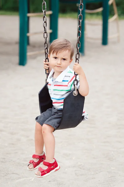 Retrato de triste chateado preocupado pequena criança menino na tshirt e jeans shorts no balanço no quintal playground fora no dia de verão, conceito de estilo de vida infantil — Fotografia de Stock