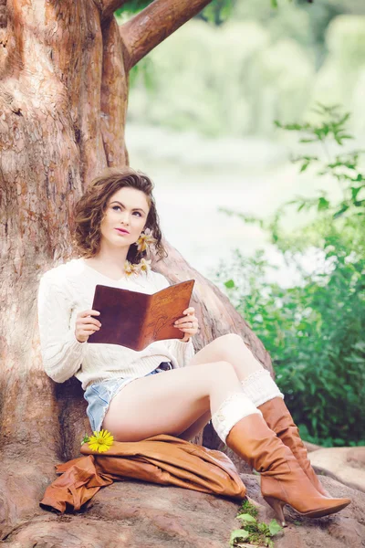 Porträtt av vackra vita kaukasiska tjej kvinna med långt mörkt rött brunt hår, i shorts och tröja, sitter i sommaren park skog utanför läsa bok drömmer, tonas titta upp, med Instagram filter — Stockfoto